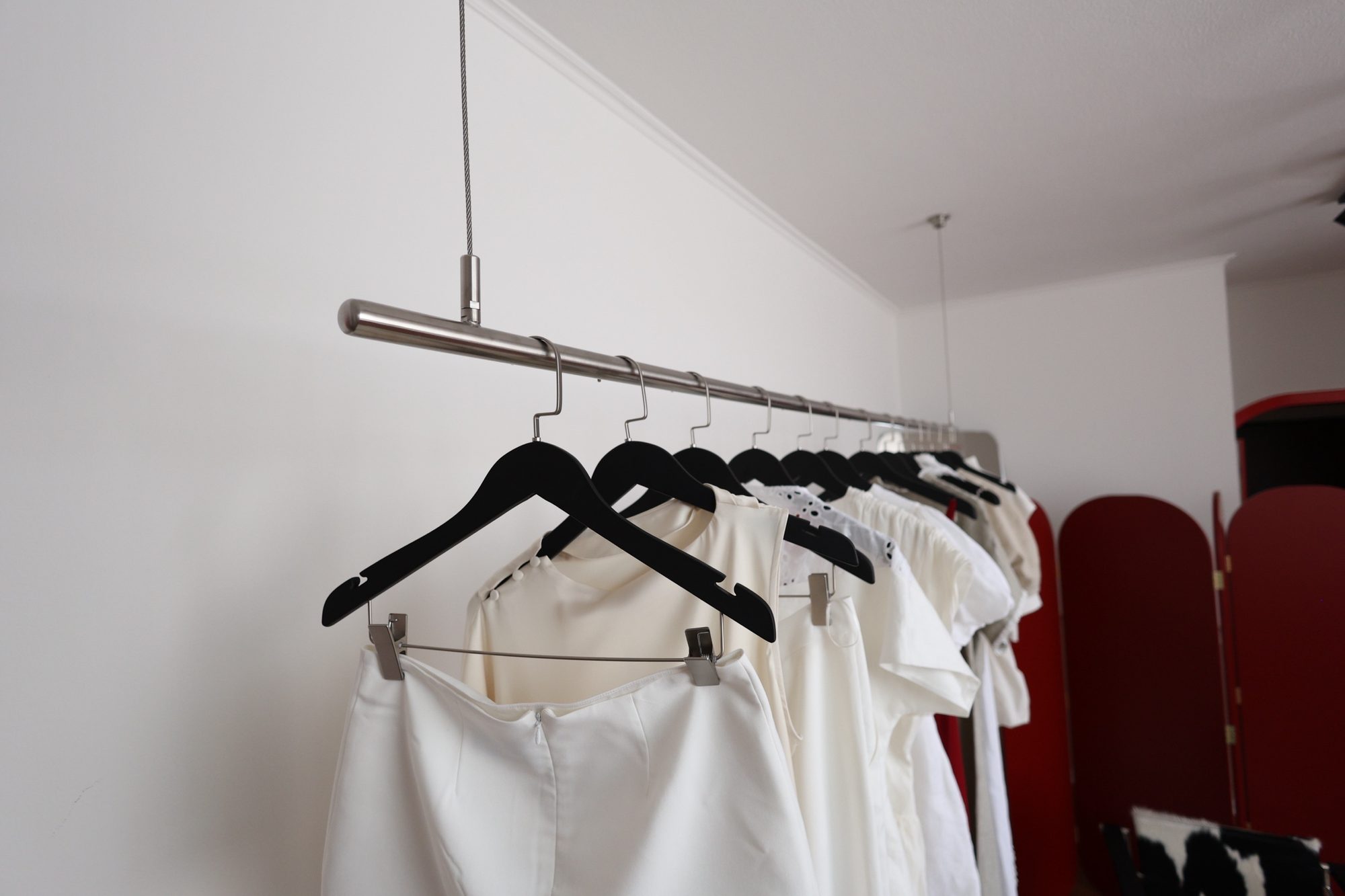 Suspended garment rail hanging from thin steel stems with hangers at Door 903