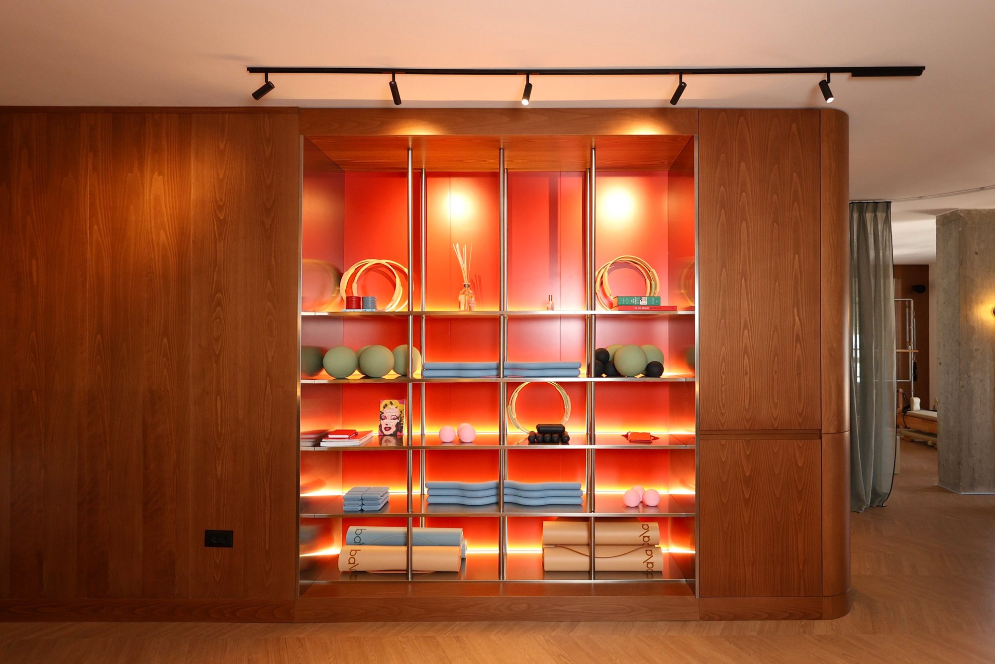 Frontal view of the illuminated stainless steel equipment wall within oak cabinetry, with pilates rings, balls and rolled mats at La Suite