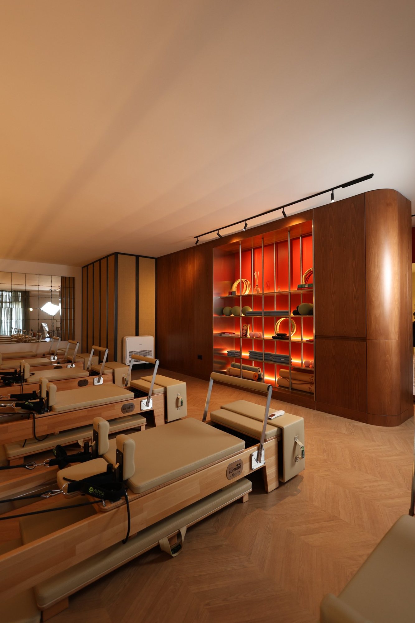 Pilates reformers arranged beside the illuminated steel equipment wall in its oak frame, with a mirrored wall at La Suite studio