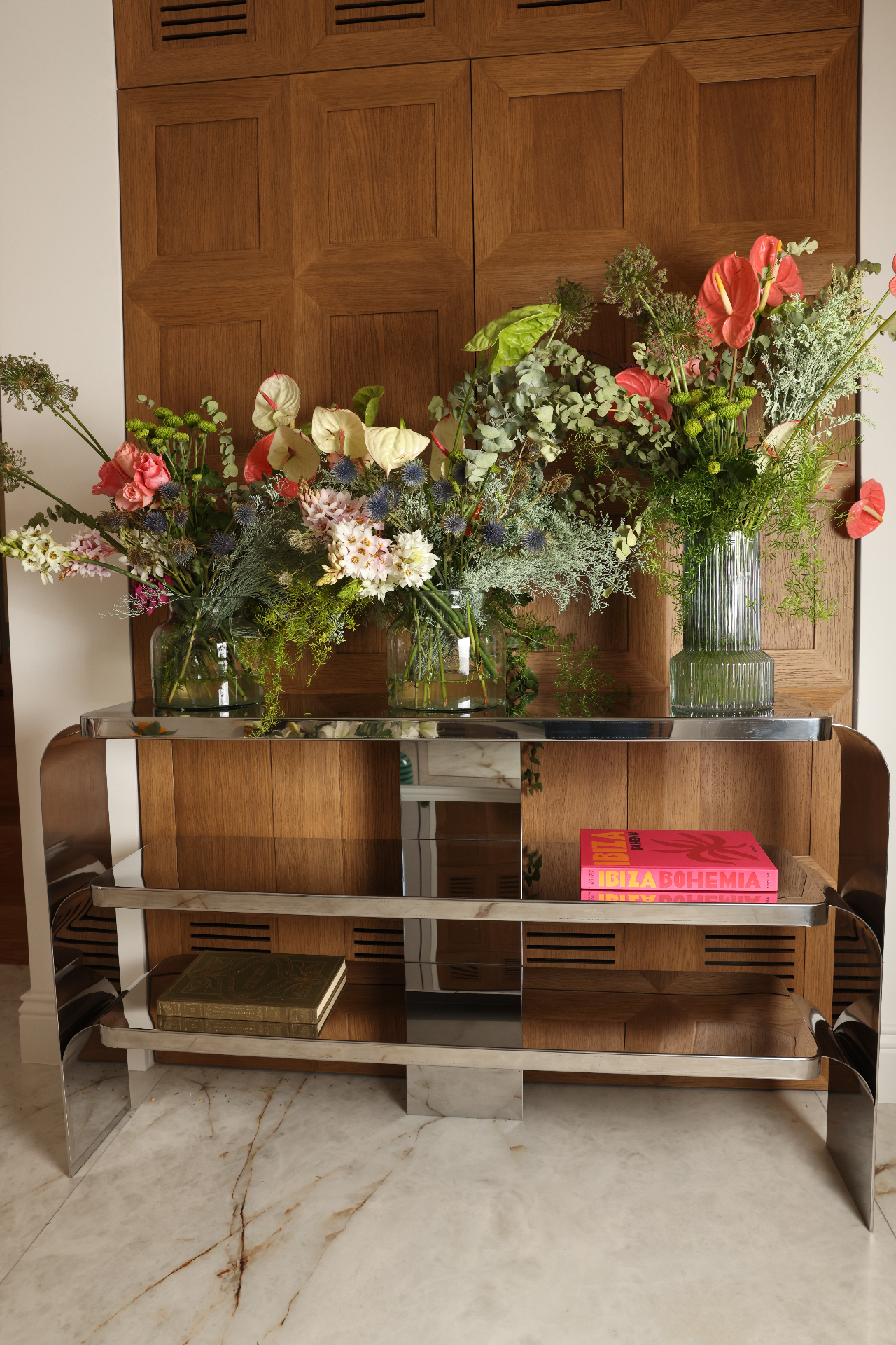 Three-plane mirror-polished stainless steel entrance console with flowers at Villa Allegra